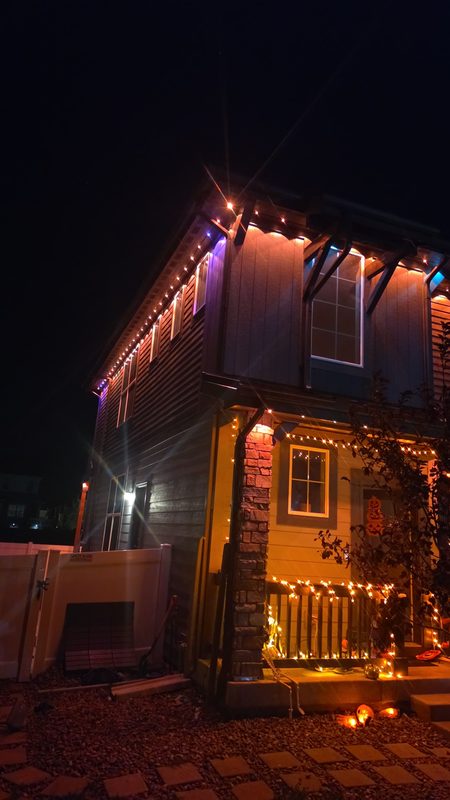 Halloween: amber and purple on the corner, porch wrapped in warm lights